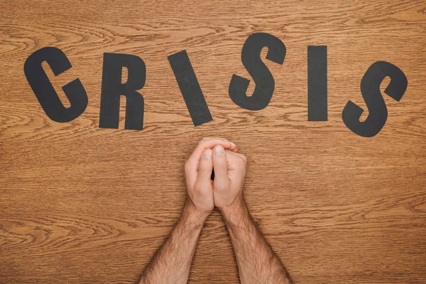 Partial view of male folded hands near black paper cut word crisis on wooden desk — Stock Photo