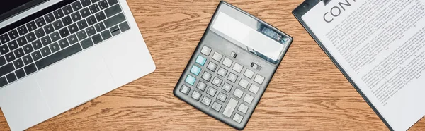 Top view of calculator, laptop and clipboard with contract on wooden desk, panoramic shot — Stock Photo