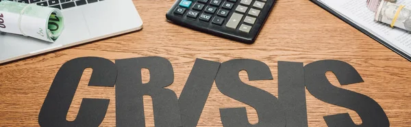 Tiro panorâmico de papel cortar crise palavra, laptop, calculadora, rolos de dinheiro de notas de dólar e euro em mesa de madeira — Fotografia de Stock