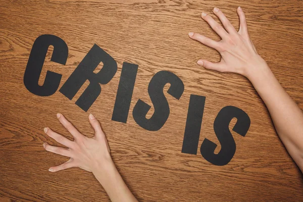 Cropped view of female hands near black paper cut word crisis on wooden floor — Stock Photo