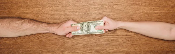 Cropped view of man and woman holding dollar banknote on wooden surface, panoramic shot — Stock Photo