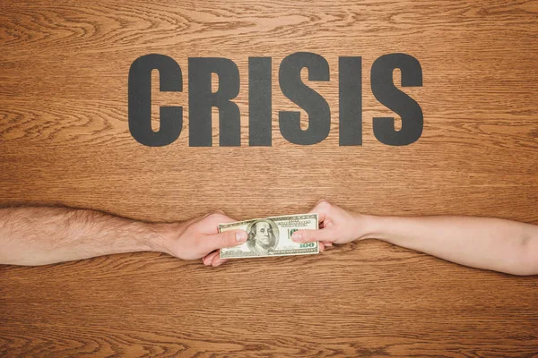 Partial view of man and woman holding dollar banknote near black paper cut word crisis on wooden surface — Stock Photo