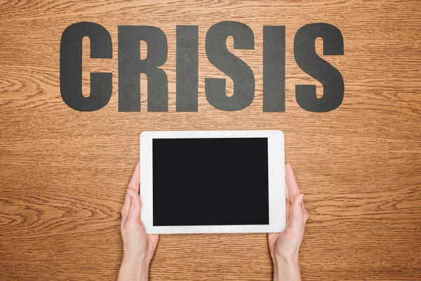 Cropped view of woman holding digital tablet with blank screen near black paper cut word crisis on wooden desk — Stock Photo