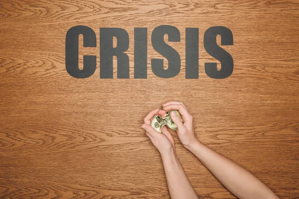 Cropped view of female hands with dollar banknote near black paper cut word crisis on wooden desk — Stock Photo