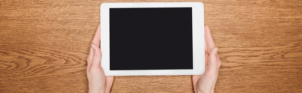 Cropped view of woman holding digital tablet with blank screen on wooden desk, panoramic shot — Stock Photo