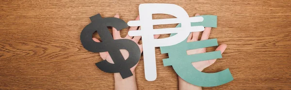 Cropped view of woman holding dollar, peso and euro paper cut symbols on wooden desk, panoramic shot of — Stock Photo