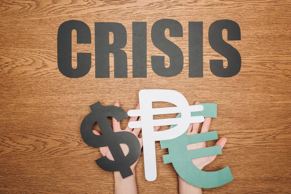 Cropped view of woman holding dollar, peso and euro paper cut symbols, and word crisis on wooden desk — Stock Photo