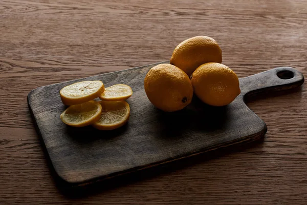 Limones enteros amarillos maduros y cortados sobre tabla de cortar sobre fondo de madera - foto de stock