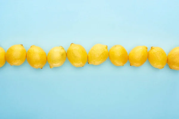 Flat lay with ripe yellow lemons in line on blue background — Stock Photo