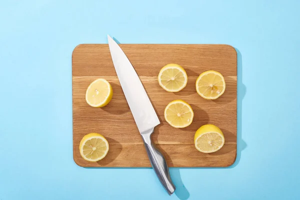 Vista superior de limones maduros de corte amarillo sobre tabla de cortar de madera con cuchillo sobre fondo azul - foto de stock