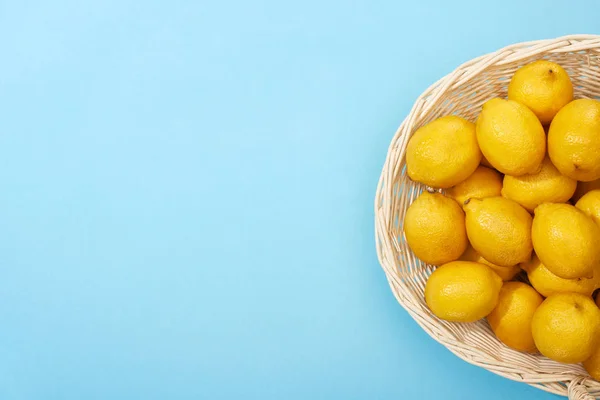 Vista superior de limones amarillos maduros en canasta de mimbre sobre fondo azul con espacio para copiar - foto de stock