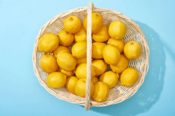 Верхний вид спелых желтых лимонов в плетеной корзине на синем фоне — стоковое фото
