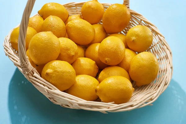 Ripe yellow lemons in wicker basket on blue background — Stock Photo