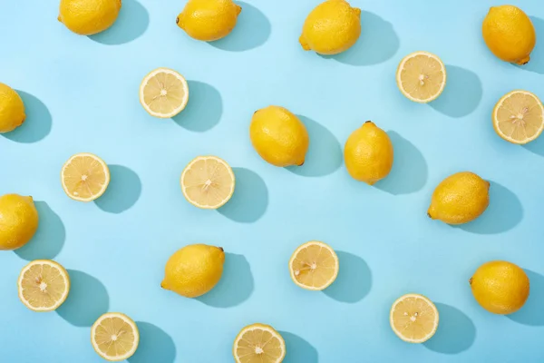 Vue de dessus de citrons jaunes entiers et coupés sur fond bleu — Photo de stock