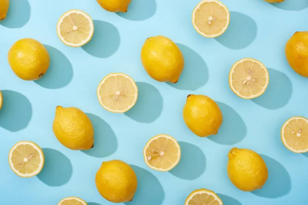 Vue de dessus de citrons jaunes entiers et coupés sur fond bleu — Photo de stock