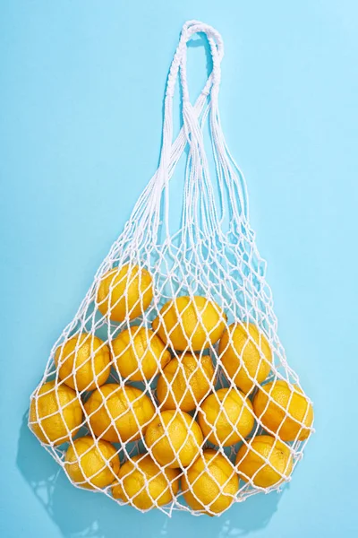 Top view of ripe yellow lemons in string bag on blue background — Stock Photo