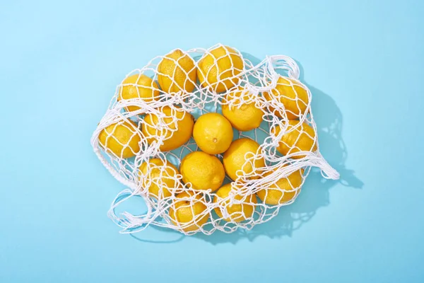 Vue du dessus des citrons jaunes mûrs dans un sac à ficelle sur fond bleu — Photo de stock
