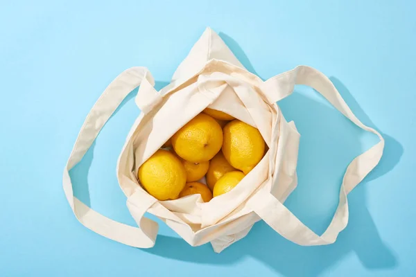 Вид зверху на стиглі жовті лимони у бавовняній еко сумці на синьому фоні — стокове фото