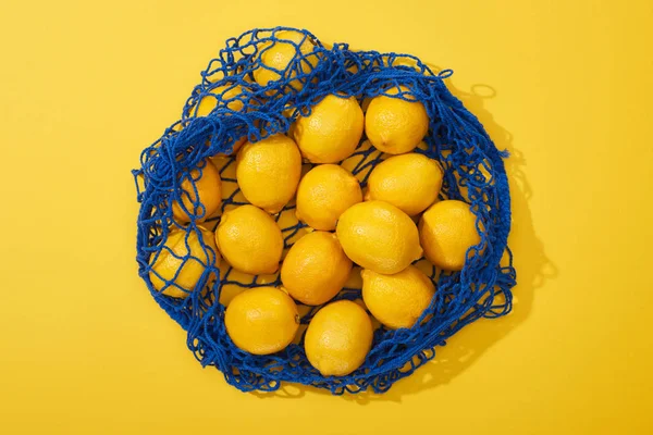 Top view of ripe lemons in string bag on yellow background — Stock Photo