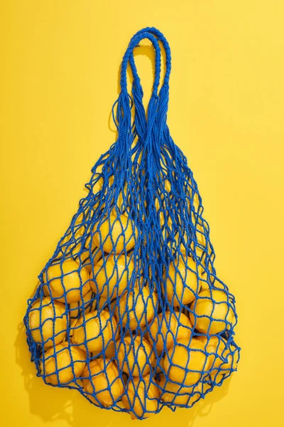 Top view of ripe lemons in string bag on yellow background — Stock Photo