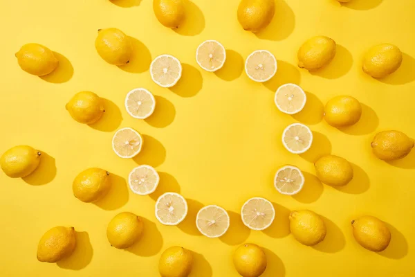 Vue de dessus de coupe mûre et de citrons entiers disposés en cadre rond sur fond jaune avec espace de copie — Photo de stock