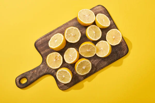 Vue du dessus des citrons coupés mûrs sur planche à découper en bois sur fond jaune — Photo de stock