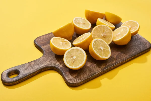 Reife geschnittene Zitronen auf Holzschneidebrett auf gelbem Hintergrund — Stockfoto