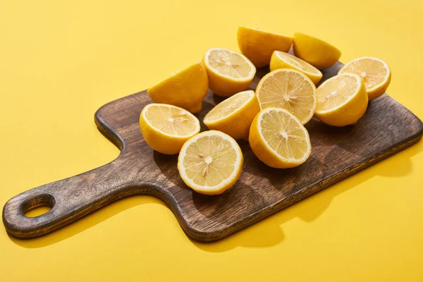 Ripe cut lemons on wooden cutting board on yellow background — Stock Photo