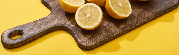Ripe cut lemons on wooden cutting board on yellow background, panoramic shot — Stock Photo