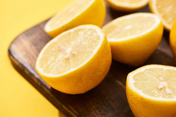 Vista de cerca de limones cortados maduros sobre tabla de cortar de madera sobre fondo amarillo - foto de stock