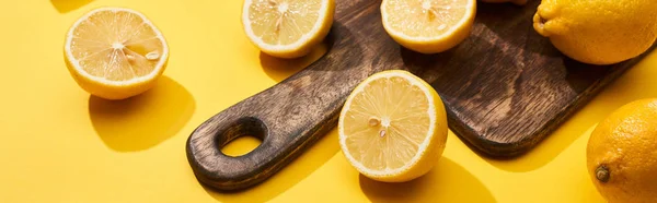 Limoni tagliati maturi su tagliere di legno su fondo giallo, colpo panoramico — Foto stock