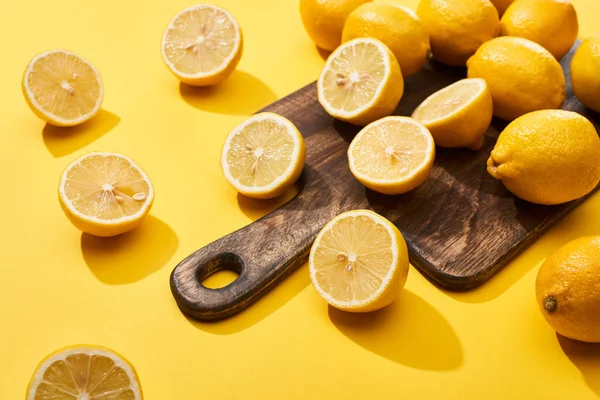 Reife geschnittene und ganze Zitronen auf Holzschneidebrett auf gelbem Hintergrund — Stockfoto