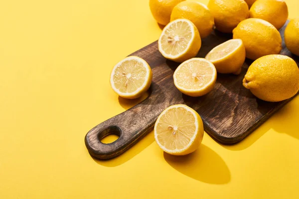 Corte maduro y limones enteros sobre tabla de cortar de madera sobre fondo amarillo con espacio para copiar — Stock Photo