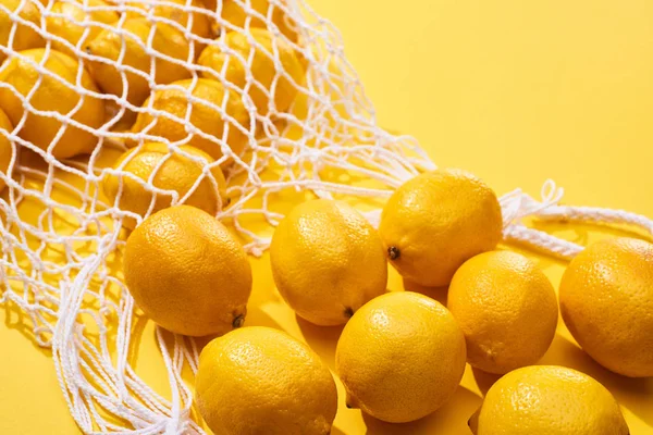 Fresh ripe whole lemons in eco string bag on yellow background — Stock Photo