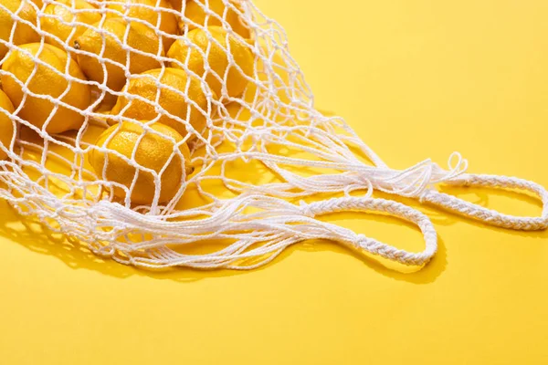 Fresh ripe whole lemons in eco string bag on yellow background — Stock Photo