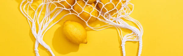 Top view of fresh ripe whole lemons in eco string bag on yellow background, panoramic shot — Stock Photo
