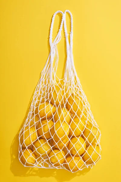 Vista superior de limones enteros maduros frescos en bolsa de hilo ecológico sobre fondo amarillo - foto de stock
