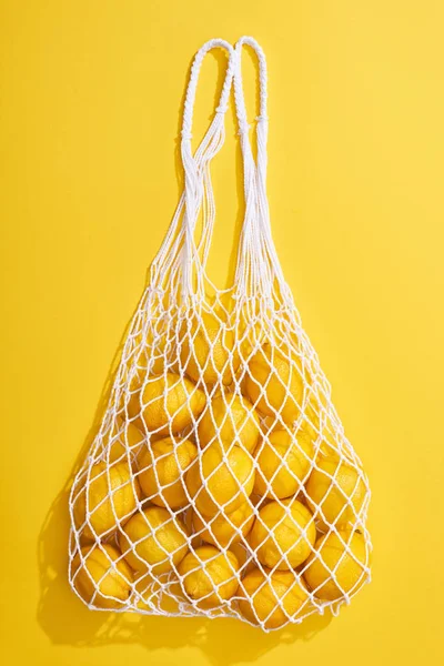 Top view of fresh ripe whole lemons in eco string bag on yellow background — Stock Photo