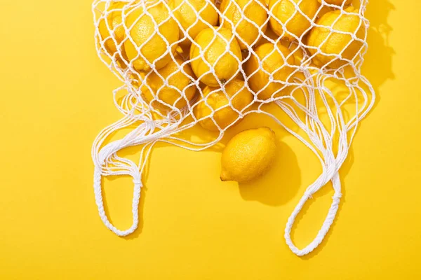 Верхний вид свежих спелых целых лимонов в эко-мешок струны на желтом фоне — стоковое фото