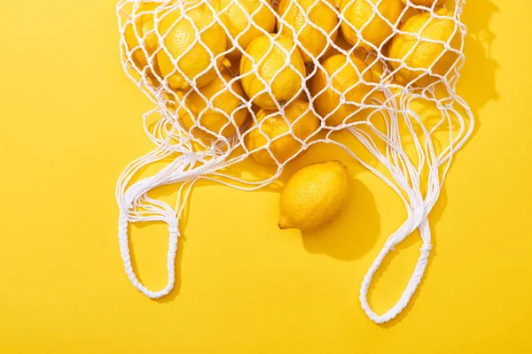 Vista superior de limones enteros maduros frescos en bolsa de hilo ecológico sobre fondo amarillo - foto de stock