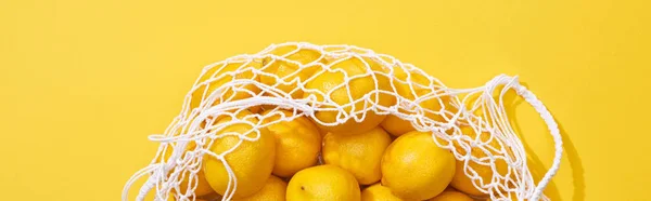 Top view of fresh ripe whole lemons in eco string bag on yellow background, panoramic shot — Stock Photo