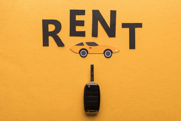 Top view of car key, paper cut auto and black rent lettering on orange background — Stock Photo