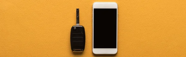 Top view of car key and smartphone with blank screen on orange background with copy space, panoramic shot — Stock Photo