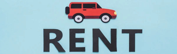 Top view of paper cut car and black rent lettering on blue background, panoramic shot — Stock Photo