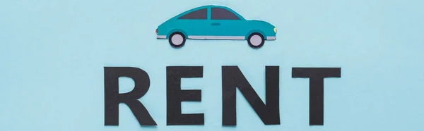 Top view of paper cut car and black rent lettering on blue background, panoramic shot — Stock Photo