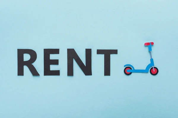 Top view of paper cut kick scooter and black rent lettering on blue background — Stock Photo