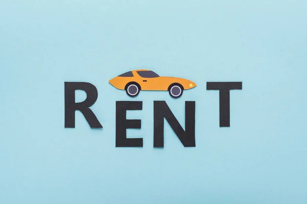 Top view of paper cut sports car and black rent lettering on blue background — Stock Photo