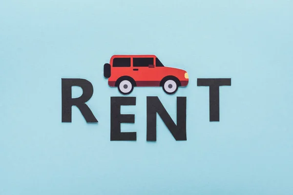 Top view of paper cut car and black rent lettering on blue background — Stock Photo