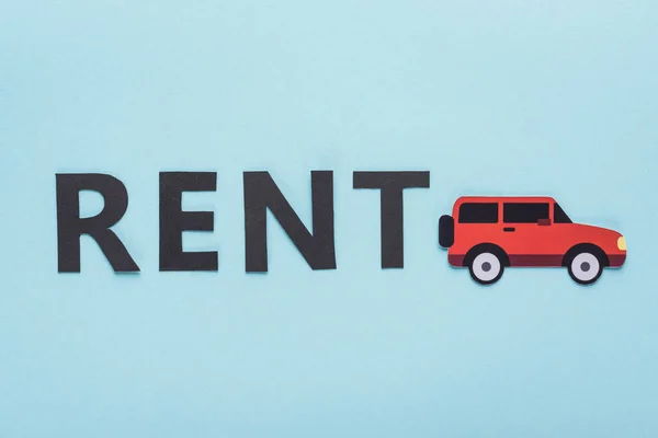 Top view of paper cut car and black rent lettering on blue background — Stock Photo