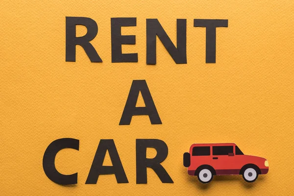 Draufsicht auf Papier geschnittenes Fahrzeug und schwarzer Rent a Car Schriftzug auf orangefarbenem Hintergrund — Stockfoto